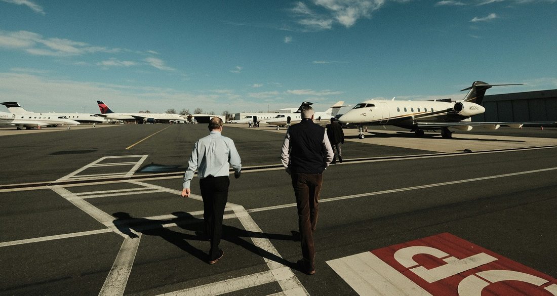 Twee mannen die lopen over een luchthaven met privéjets