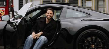 Zanger Rolf Sanchez zit met zijn benen naar buiten in zijn net nieuwe Porsche 911 Carrera T