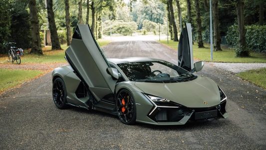 De Lamborghini Revuelto van Marktplaats met zijn vleugeldeuren open op een bospad