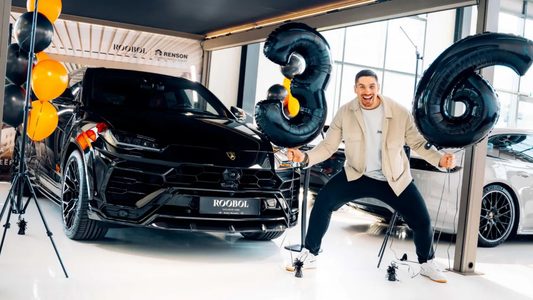 Rico Verhoeven poseert blij bij zijn nieuwe Lamborghini Urus met ballonnen met het cijfer 36 eromheen