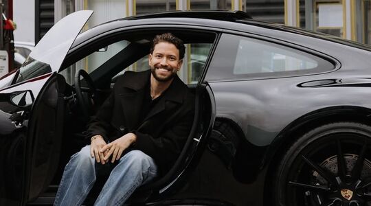 Zanger Rolf Sanchez zit met zijn benen naar buiten in zijn net nieuwe Porsche 911 Carrera T