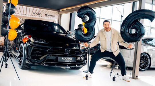 Rico Verhoeven poseert blij bij zijn nieuwe Lamborghini Urus met ballonnen met het cijfer 36 eromheen